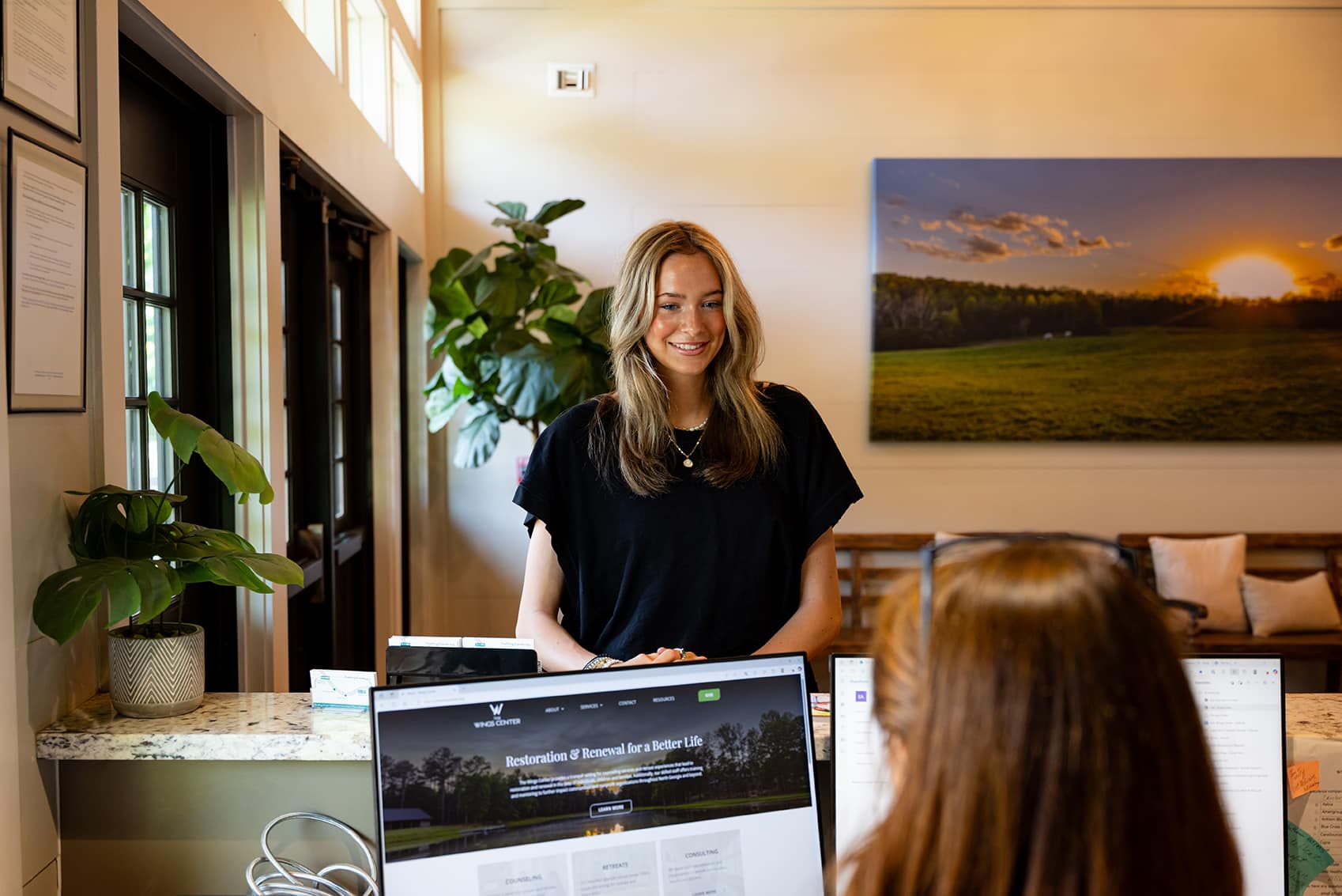 Smiling woman speaking to a receptionist who is seated looking at a computer