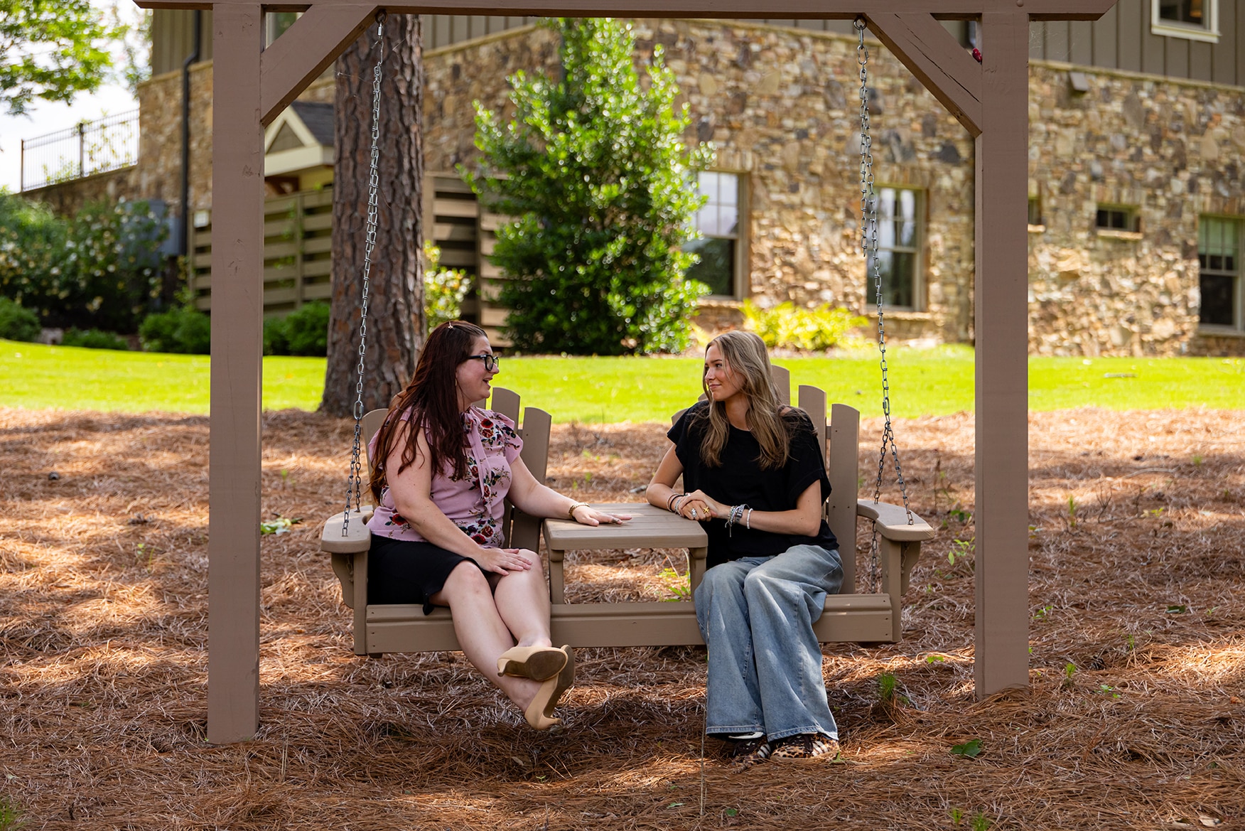 Two women talking to each other on a swing in front of a large stone building