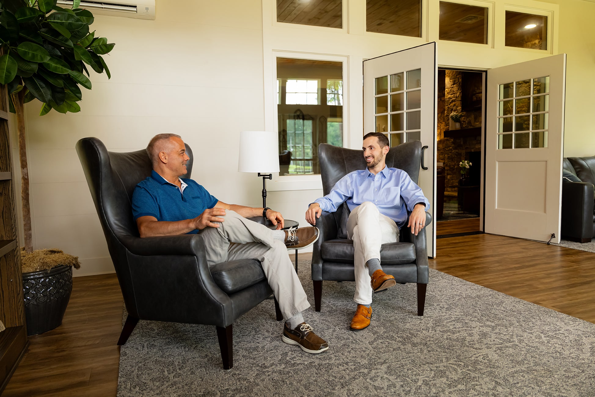 Two men in wing back chairs talking to each other in a comfortable meeting/reception area